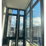 Поворотно-откидная створка тёмного ПВХ-окна с белой ручкой; двойной контур уплотнений, вид на двор зимой.