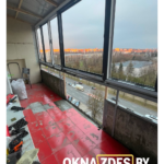 Общий вид лоджии по всей длине с тёплыми ПВХ-окнами антрацит; ночной город за стеклом.