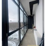 Участок лоджии с балконной дверью и верхними фрамугами; тёмные ПВХ-рамы, панорамный вид.