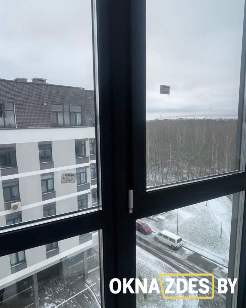 Панорамные окна вдоль лоджии, тёмные рамы; на потолке вентиляционный короб, черновая отделка.